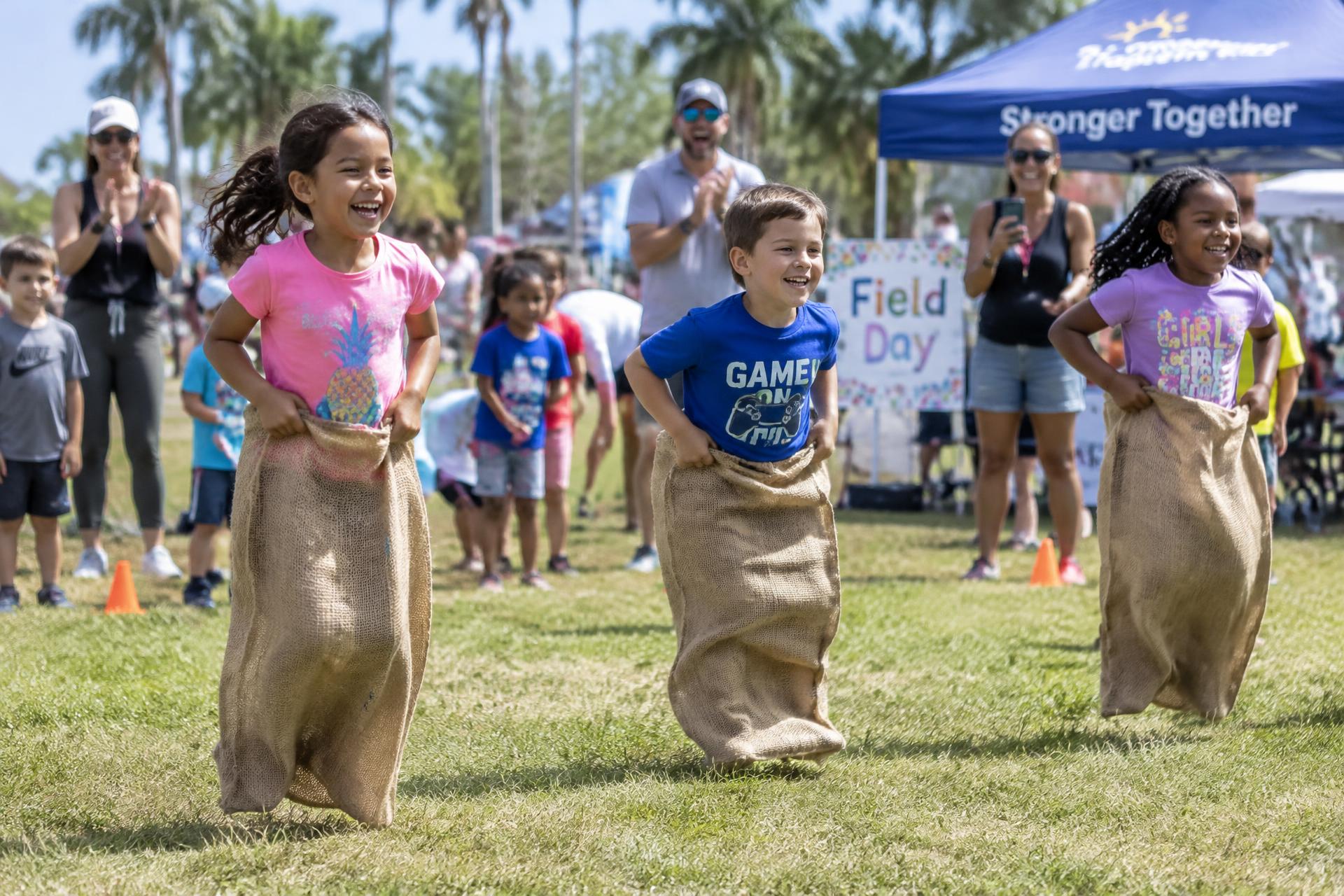 Children laughing during a sack race while parents cheer